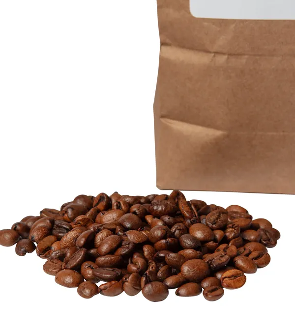 Roasted coffee beans spilling in front of a kraft paper bag