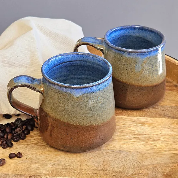Two handmade stoneware mugs in blue and brown glaze on a wooden tray